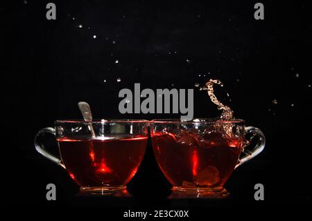 A piece of rock sugar is splashing into one of two glass cups of tea in front of a black background Stock Photo