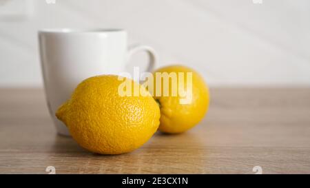 Two lemons on the kitchen table near a white mug of tea. Morning concept Stock Photo