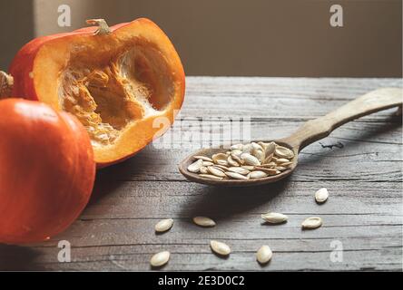Fresh organic pumpkins and pumpkin seeds in a wooden spoon on a dark wooden table close-up Stock Photo
