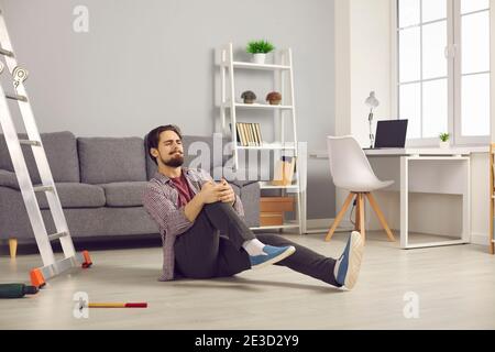 Man who's fallen from ladder and hurt his knee sitting on floor and suffering from pain Stock Photo