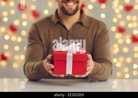 Cropped image close up of a red gift box with a white bow in male hands sitting at the table. Stock Photo