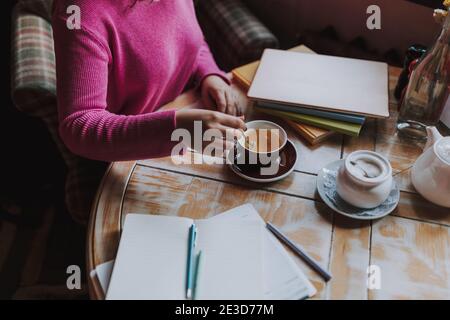 Top view of young lady studying in cafeteria and enjoying hot drink while stirring tea with a teaspoon Stock Photo