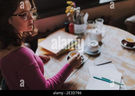 Attractive female sitting alone and stirring tea with a teaspoon while looking away in cafeteria Stock Photo
