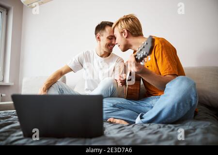 Happy gay couple sitting on bed and touching foreheads Stock Photo