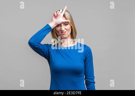 Portrait of displeased young woman in elegant tight blue dress standing with hand on forehead showing loser gesture, unemployed or fired from job. ind Stock Photo