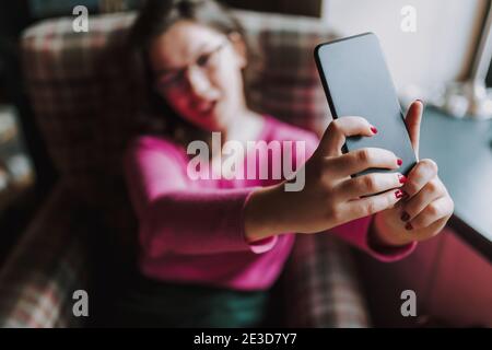 Smiling young lady posing on smartphone camera while taking selfie in cafe Stock Photo
