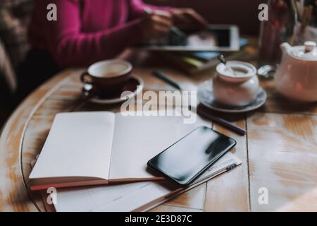 Smartphone and cup of tea on the table with woman working on the background Stock Photo