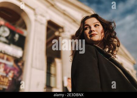 Low angle view of smiling beautiful young woman enjoying the walk on the street with building on the background Stock Photo