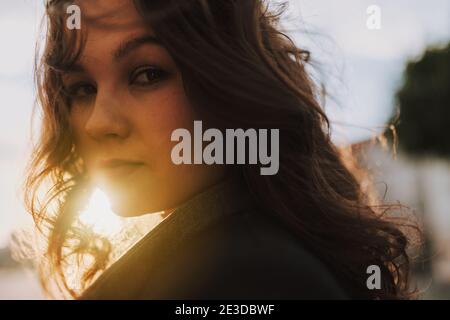 Close up of attractive brunette lady in black coat walking outdoors and looking at camera Stock Photo