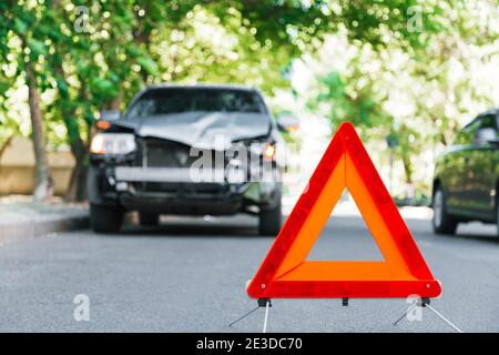 Red emergency stop triangle sign on road during a car accident. Broken gray car in road traffic accident. Car crash traffic accident on city road Stock Photo