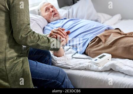 close-up photo of senior couple hands holding together, woman supports her sick husband lying on bed in hospital Stock Photo