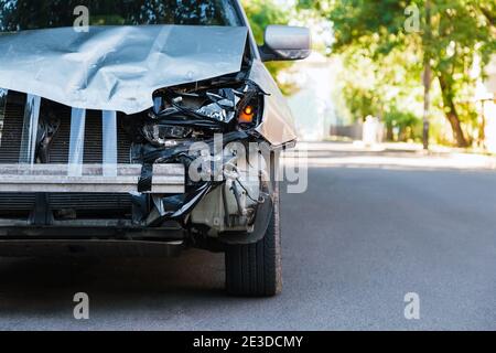 Destroyed car in car crash traffic accident on city road. Smashed broken front auto headlight, dented hood without bumper on gray car accident with Stock Photo