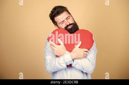 Feeling lonely and broken hearted. Bearded man holding big red heart. Valentines man expressing love on 14 february. Love sickness and heart problems. Having heart attack and heartache. Stock Photo