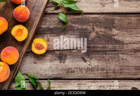 Peaches with leaves on a wooden board with peach in halves. Flat lay composition with ripe juicy peaches. Harvest of peaches for food or juice. Top Stock Photo