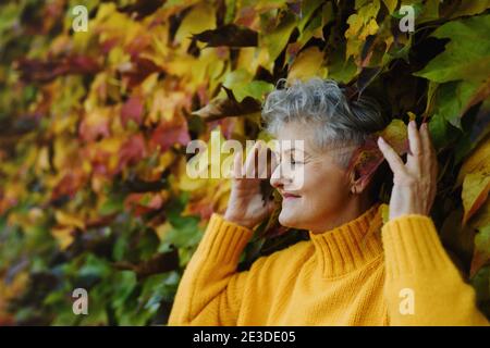 Senior woman standing outdoors against colorful natural autumn background, eyes closed. Stock Photo