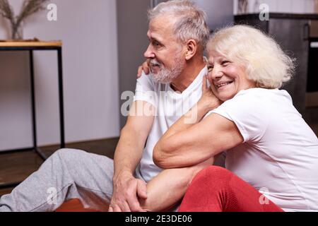 senior couple sit having rest on the floor after sport exercises together, enjoy being healthy and sportive, smile hugging Stock Photo