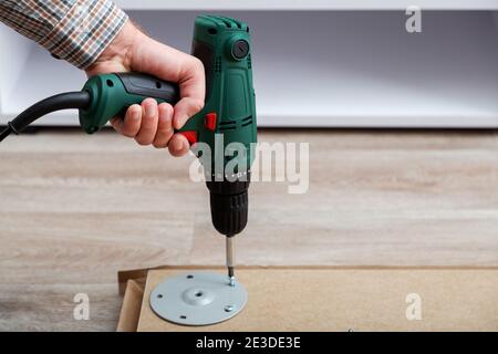 Man assembles table furniture with drill. Assembly, furniture repair home master. Male hand with drill on floor. Copy space Stock Photo