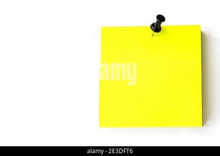 Push Pin And Yellow Note Paper Office Business. A square blank yellow note is pinned to a white wall Stock Photo