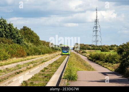 A bus passes a cyclist near the Gravel Bridge Road transmitter mast on the Cambridgeshire Guided Busway. Stock Photo