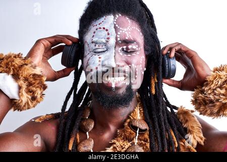 african native man in ethnic wear enjoy music in headphones, smile at camera isolated over white background, standing with eyes closed Stock Photo