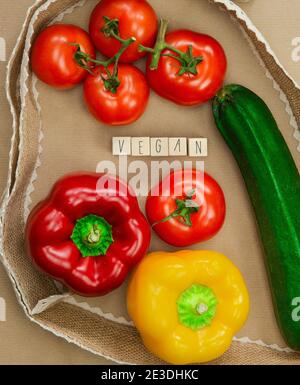 Vegan written with wooden cubes surrounded with fresh organic vegetables on brown craft paper with natural burlap ribbon top view, Vegan,Healthy food Stock Photo