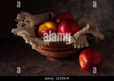 Ripe and juicy nectarines in a bowl on a table on a dark background.  Stock Photo