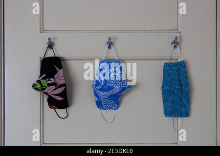 Three covid-19 cloth face masks hanging on door hooks at home ready to wear before leaving the house. Front view close-up