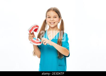 Smiling girl in a blue uniform showing how to properly brush her teeth using an anatomical model of jaw and a toothbrush. Isolated on white Stock Photo