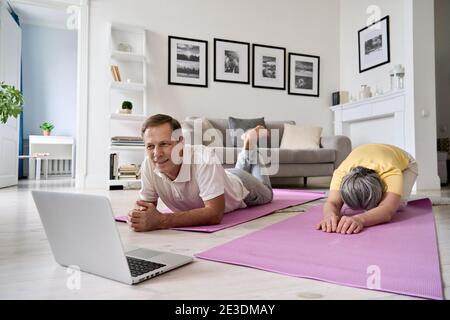 Healthy mature couple watching online yoga fitness class exercising at home. Stock Photo