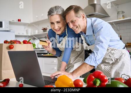 Happy old couple using laptop holding credit card order food in grocery online. Stock Photo