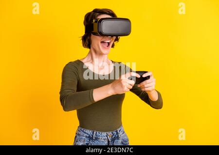 Beautiful girl play video game with joystick in vr goggles wear green denim sweater isolated on shine yellow color background Stock Photo
