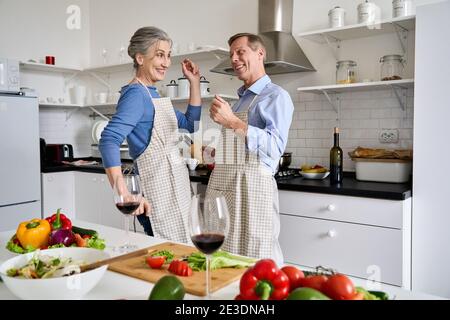 Active happy old mature couple enjoying dancing and cooking together at home. Stock Photo