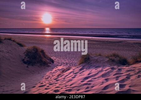 Small path leading from marram grass covered dunes towards the beach prior to a colorful sunset Stock Photo