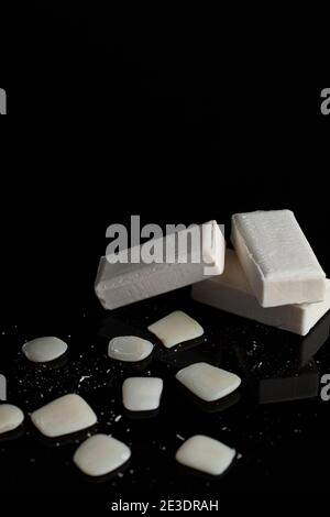 white bars of soap are stacked on top of each other with leftover soap slieves and pieces lying around on reflective dark surface. A concept image for Stock Photo