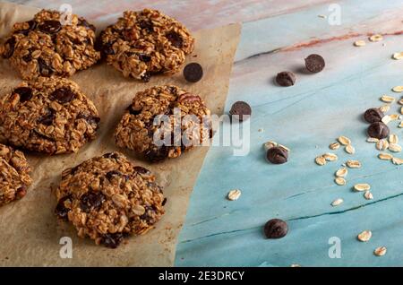 Fresh out of oven homemade cookies on baking paper of green marble countertop. Dark Chocolate chips and rolled oats are seen on the surface. A healthy Stock Photo