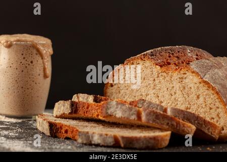 Close up side view image of a freshly baked thick crust sourdough artisan bread with an active rising sourdough starter culture in the background. Ris Stock Photo