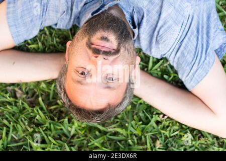 Adult caucasian man lying upside down portrait on grass Stock Photo