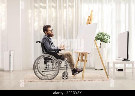 Male artist in a wheelchair painting on a canvas at home Stock Photo