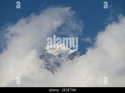 Snow covered mountain peak with summit cross peeking through clouds Stock Photo