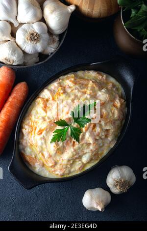 Carrot tarator in ceramic bowl with vegetable on dark background. Fresh carrot salad with garlic yogurt in bowl. Stock Photo