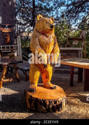 A wood carving sculpture of a smiling bear is exhibited on a tree stump in a Southern California forest while illuminated by a sun beam. Stock Photo