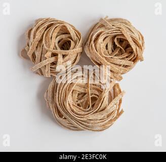 Raw whole grain brown pasta on a white background. Delicate wholemeal pasta made of graham flour, rich in nutrients protein, carbohydrates and fiber Stock Photo