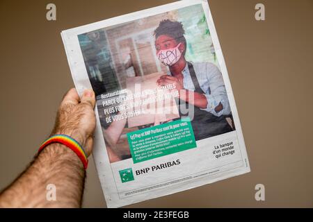 Paris, France - Jan 7, 2020: POV male hand holding newspaper with advertising in French language for the BNP Paribas bank for services like Lyf Pay during COVId-19 pandemic Stock Photo