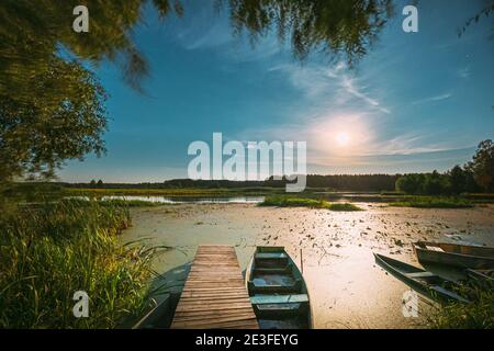 Real Night Sky Stars And Moonrise Above Old Pier With Moored Wooden Fishing Boat. Natural Starry Sky And Countryside Landscape With Lake River In Stock Photo