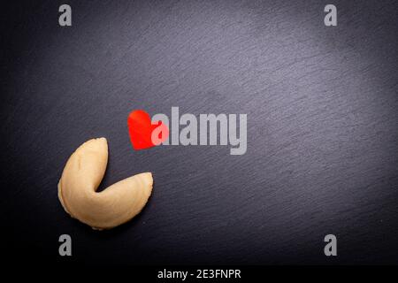 A fortune cookie with a little red heart on a black stone background. Are you ready to break the cookie and discover your love destiny? Stock Photo