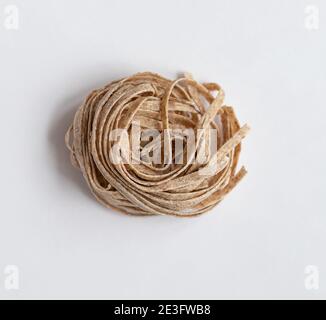 One portion raw whole grain brown pasta on a white background. Delicate wholemeal pasta made of graham flour Stock Photo