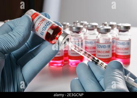 Doctors hand in protective gloves holds vaccine vial and fill syringe Stock Photo