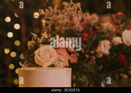 wedding cake decorated with pink flowers on a wooden table with background lights. Stock Photo