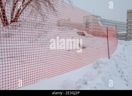 Plastic red safety net for construction site. Fencing repair work on the street. Construction grid on the background of winter snow Stock Photo