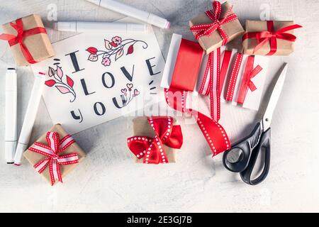 Red ribbons, gifts, scissors, markers next to valentine with words I love you . Preparation for Valentine's Day. Valentine's day concept. Flat lay. Top view